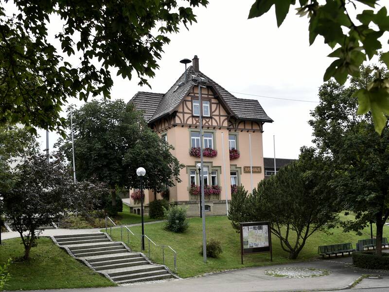 Bild des Rathauses inmitten von viel grün, überwiegend Bäume und Wiese