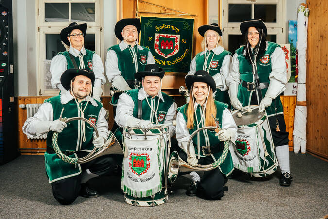 Sieben Personen des Fanfarenzugs welche in zwei Reihen vor der Flagge Durchhausens mit ihren Instrumenten stehen